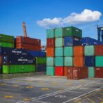 total truck support services truck - A shipping yard filled with stacks of colorful containers under a blue sky with scattered clouds. Cranes are visible in the background.