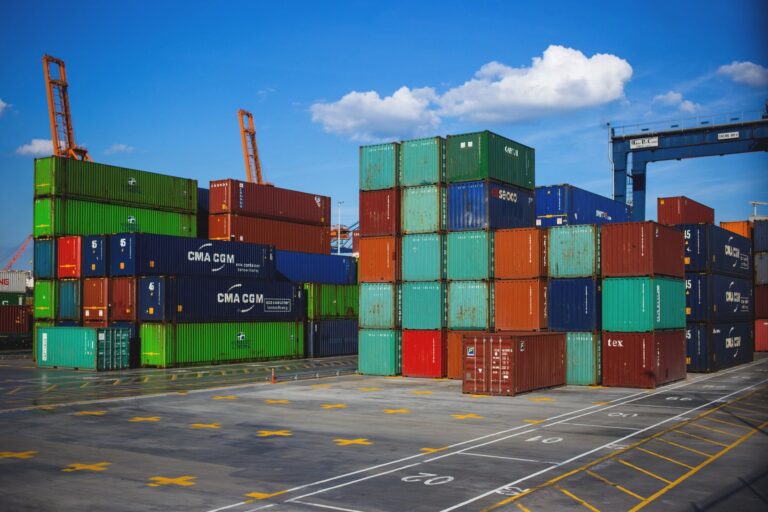 total truck support services truck - A shipping yard filled with stacks of colorful containers under a blue sky with scattered clouds. Cranes are visible in the background.